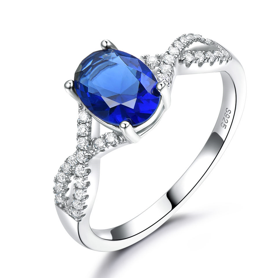 Alphalurent Infinity Azure Ring – Oval-Cut Sapphire Blue Crystal in S925 Model_s Hand Alphalurent 925 sterling silver ring featuring a vibrant oval-cut crystal center stone on a sparkling twisted infinity band, shown surrounded by white pearls. Available in blue, green, light blue, pink, and white.