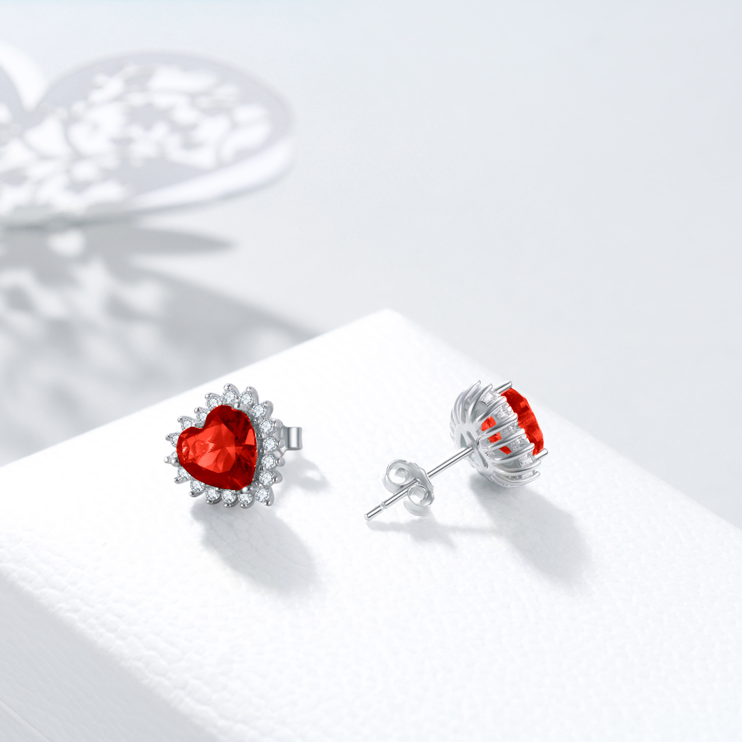 Alphalurent Crimson Heart Halo Stud Earrings | Red Zirconia in White Gold Plated 925 Silver Alphalurent 925 sterling silver stud earrings featuring a vibrant red heart-shaped cubic zirconia surrounded by a sparkling white halo. (For the model image): Model wearing Alphalurent white gold plated silver earrings with a red heart halo design.