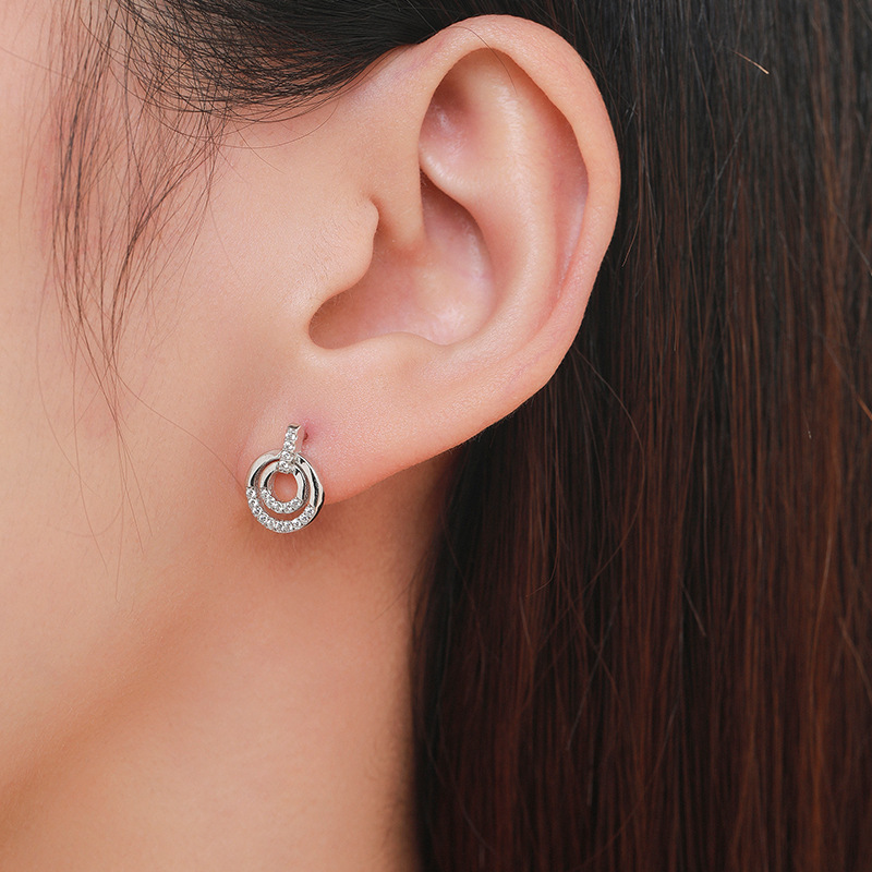Alphalurent 925 sterling silver stud earrings featuring a geometric design with two interlocking circles, accented with sparkling pave crystals.
